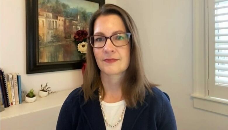 A woman with brown hair to her shoulders and glasses sits in her office for a Zoom call.