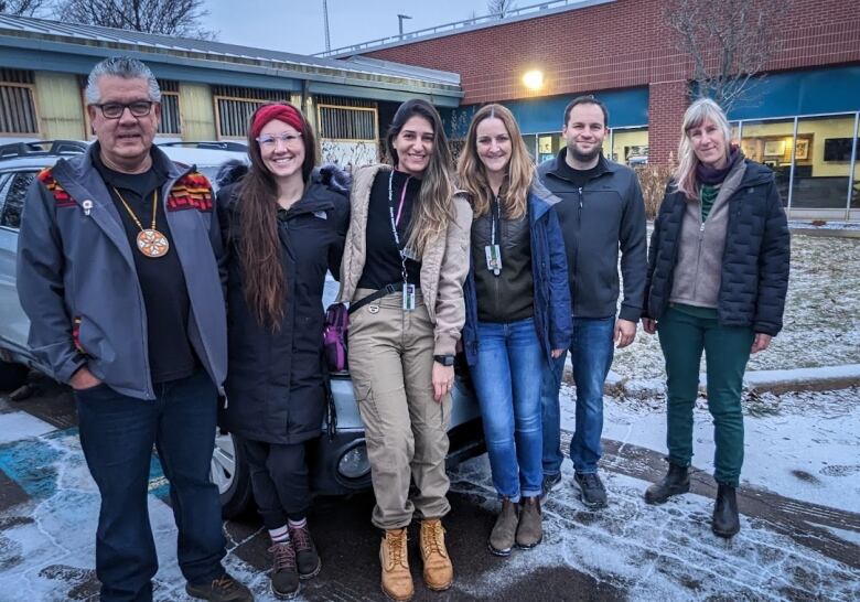 Six people stand in front of the Atlantic Veterinary College next to the car that is transporting the eagle to Nova Scotia. 