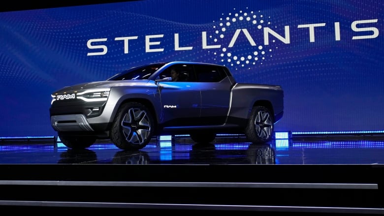 A blue pickup truck on a stage with the word Stellantis behind it.