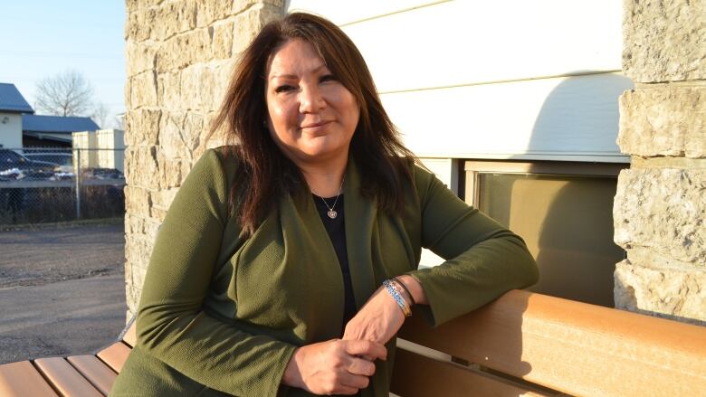 A woman sits on the bench with her hands clasped and looks at the camera.