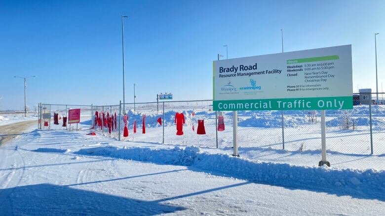 Red dresses hang on a fence next to a sign at an entry to a landfill.