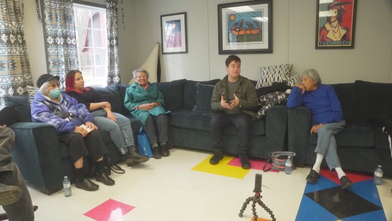 Man and four women sit on couches