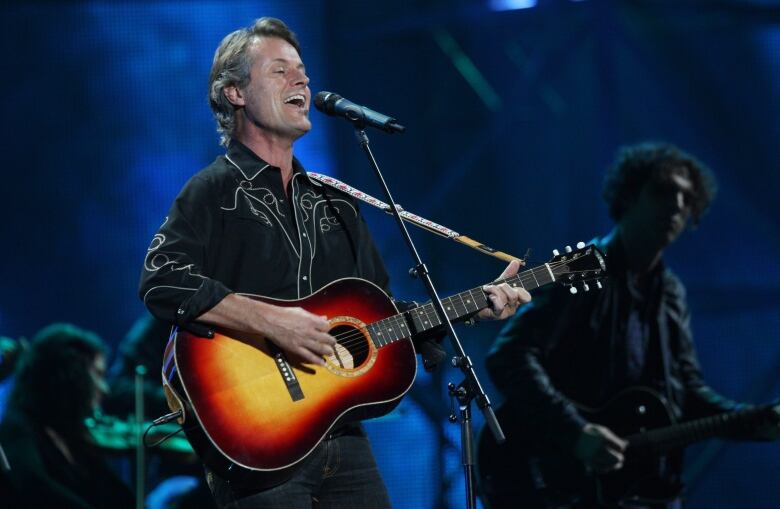 A man in a black western-style shirt plays a guitar and sings onstage.