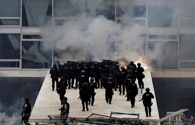 Police in riot gear storm a building.