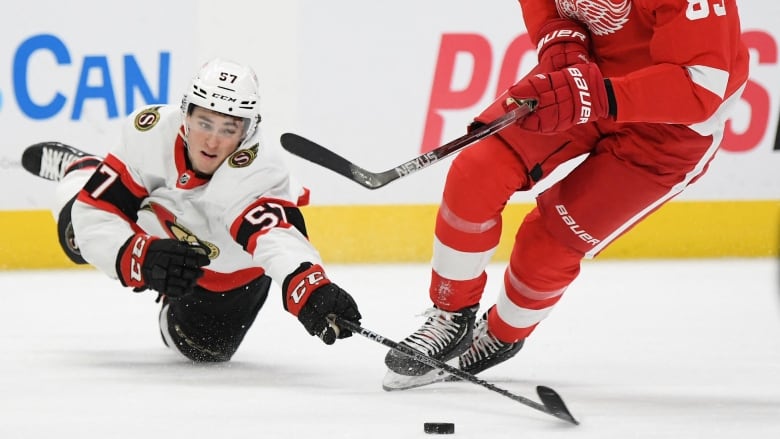 A hockey player stretches onto his stomach to try to take a puck from an opponent.