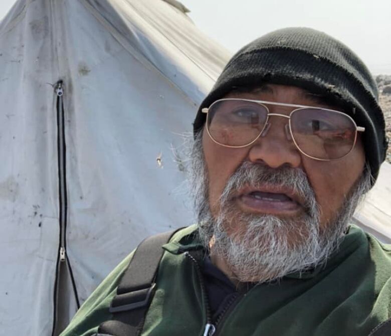 A portrait of a man. He wears a toque and glasses and has a beard.