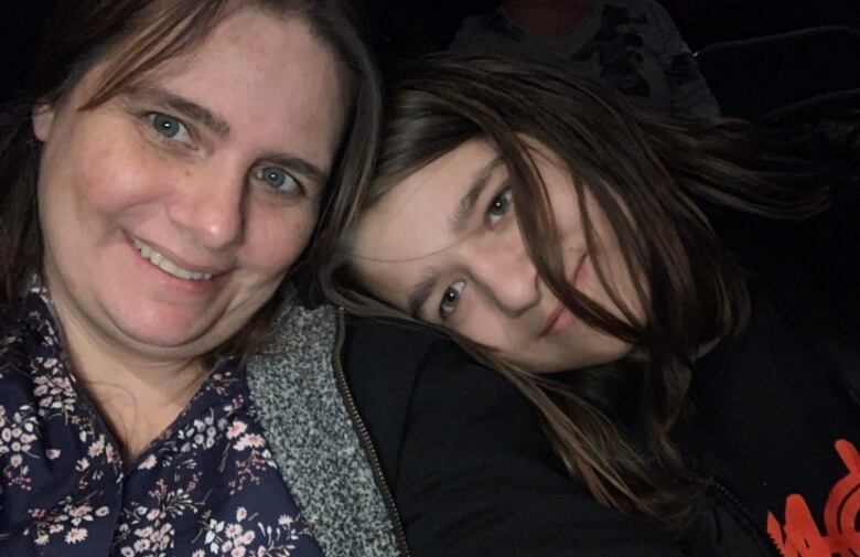 A woman in a floral shirt smiles beside her child, who leans their head on her shoulder.