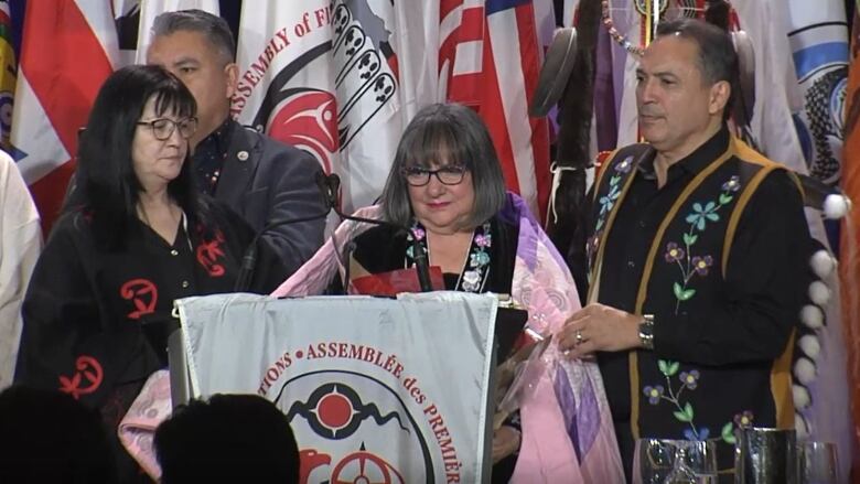 A woman on stage wears a purple and pink starblanket as others look on.