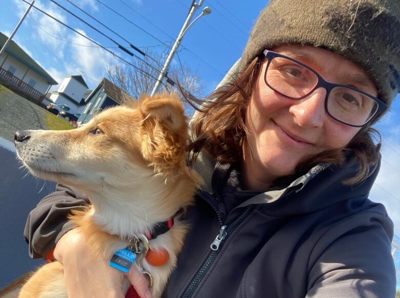 A woman wearing a grey sweater smiles while holding her dog.