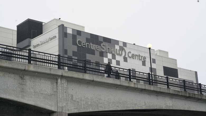 People cross a bridge with a convention centre in the background.