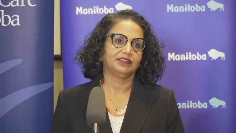 A woman with glasses stands by a podium.