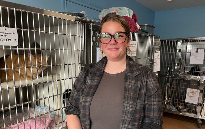 A woman stands in a room of kennels with cats inside of them. 