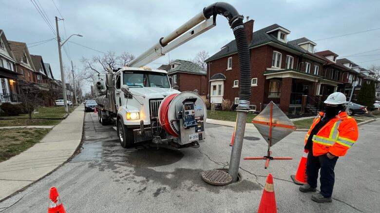 A vacuum truck has a tube going straight into a maintenance hole in the road.