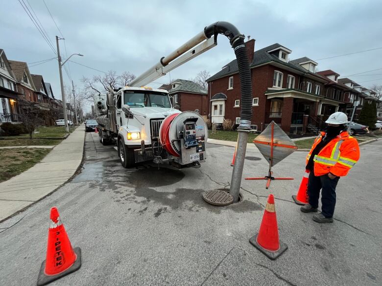 A vacuum truck has a tube going straight into a maintenance hole in the road.