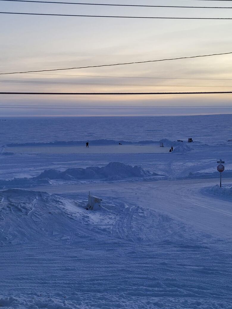 A snowy landscape with people seen distantly skating on ice.