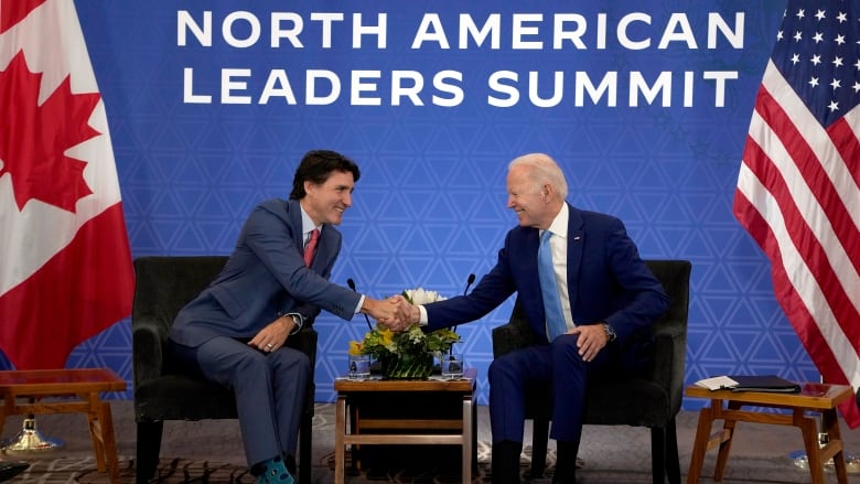 Justin Trudeau and Joe Biden smile and shake hands while seated at chairs.