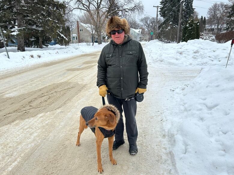 A man is standing on a street with a dog on a leash.