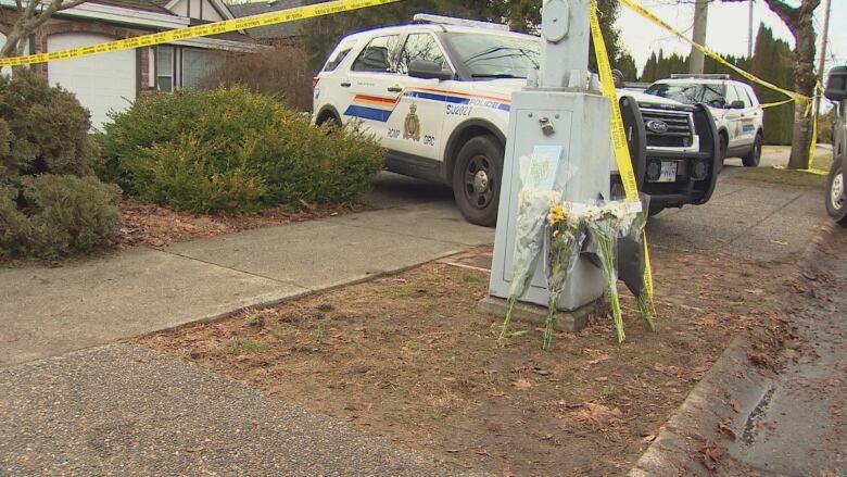 Flowers are stacked up in front of police tape and a police SUV.