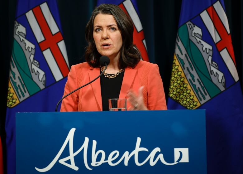 Alberta Premier Danielle Smith speaks behind a lectern bearing the provincial logo.