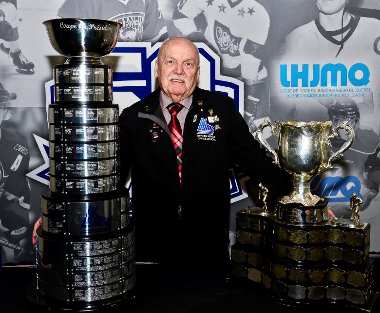 A man is standing in between two large trophies.