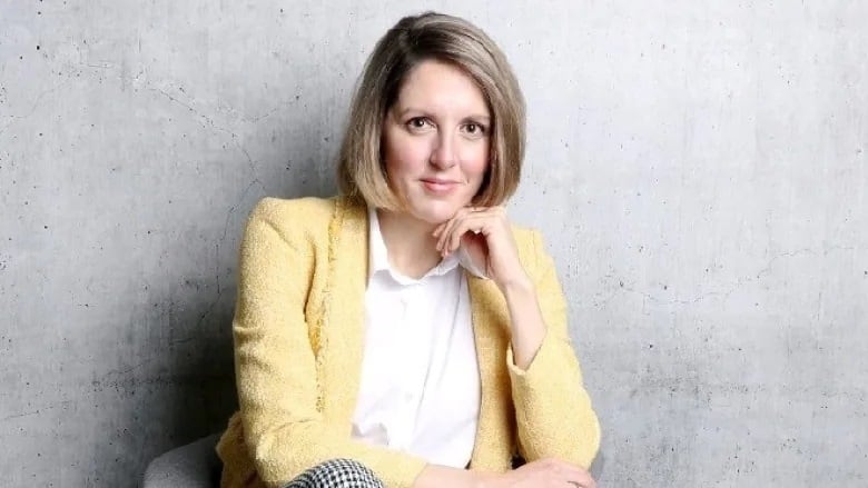 A woman looks ahead while sitting with her chin resting on her left hand.