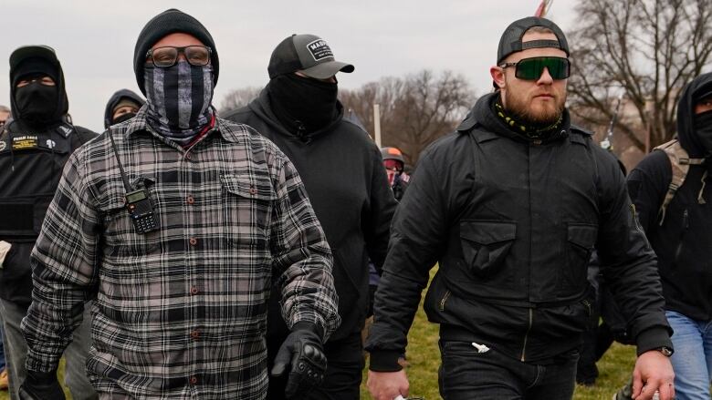 Men are seen walking on grass, one with a megaphone in his hand.