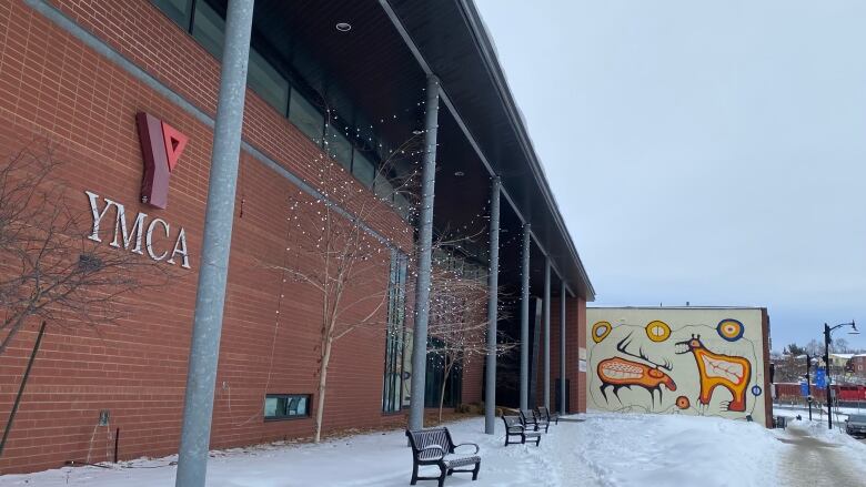 Brick building with YMCA sign in the foreground. Snow on the ground with a mural next to the building in the background. 