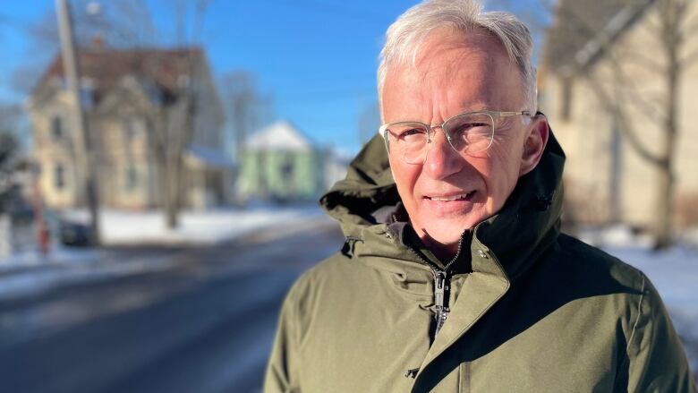 A man wearing a green parka stands on a snow-covered sidewalk. 