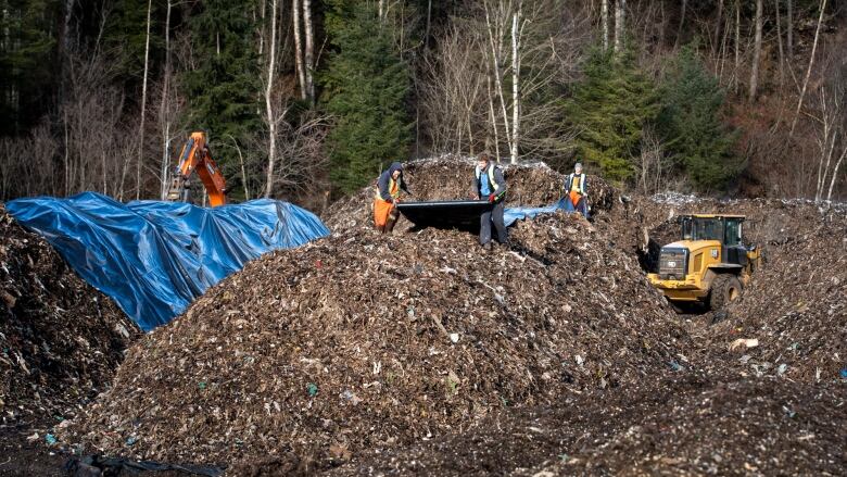 Workers apply tarps to piles of waste at a property in Columbia Valley near Cultus Lake, B.C.