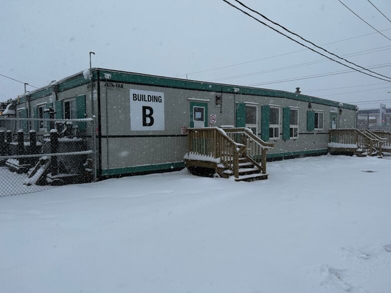 A grey one-storey building made of shipping containers is seen in a snowy landscape. 