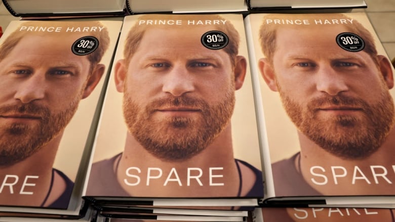 A pile of books with the cover showing a man's face sit on a table.