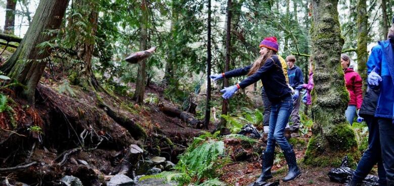 A salmon flies through the air after being tossed by a young girl in a purple jacket and pink tuque.