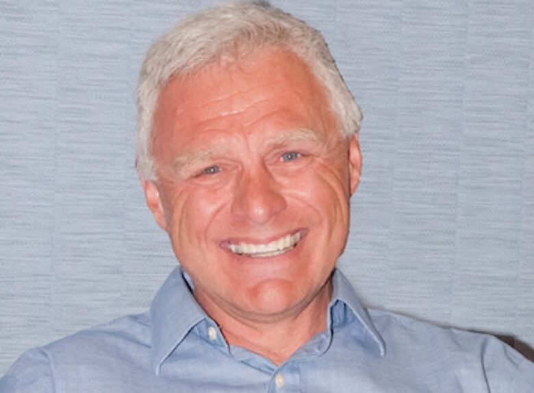 An older man with white hair in a dress shirt smiles for a portrait.