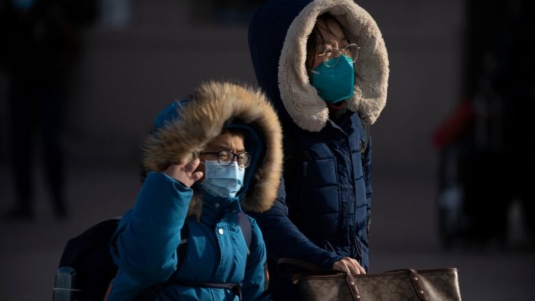 Two travellers, each wearing face masks, are seen walking toward the entrance of a railway station in Beijing on Saturday.