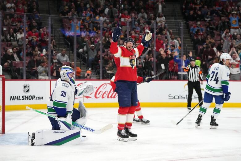 A male ice hockey player raises his arms in celebration in front of the opposing goaltender in an arena filled with cheering fans