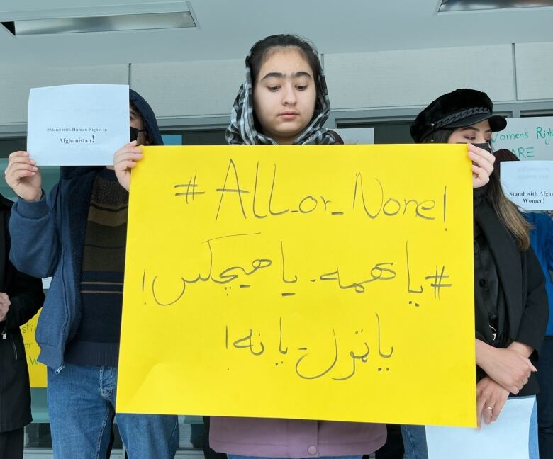 A girl wearing a hijab is holding a large poster that reads 