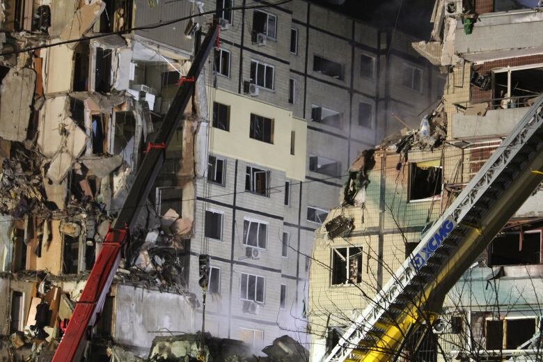 Two cranes are seen in front of a very badly damaged apartment building.