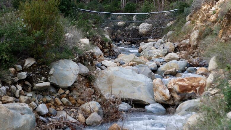 A jumble of boulders in a creek is netted off by metal cables to prevent slides.