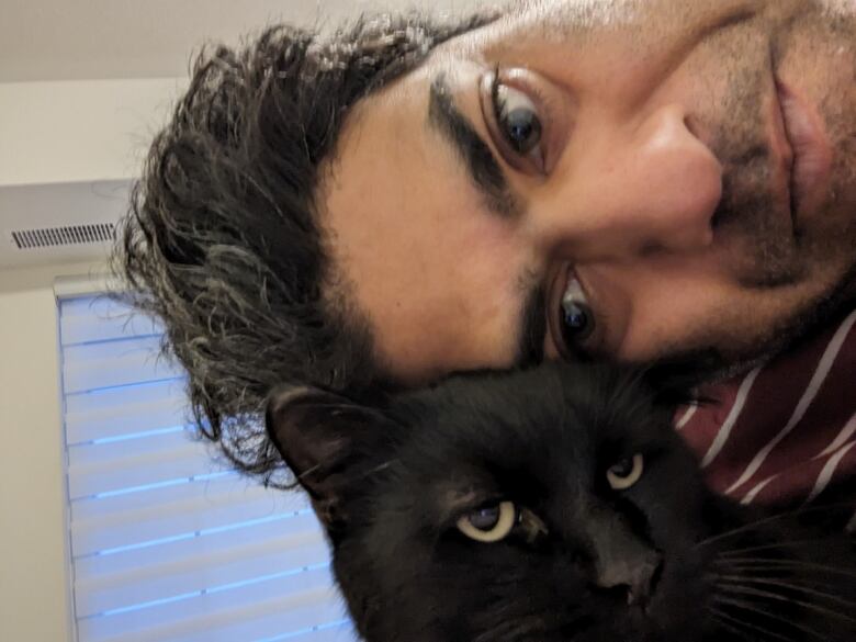 A man and a black cat looking at the camera and taking a photo together.