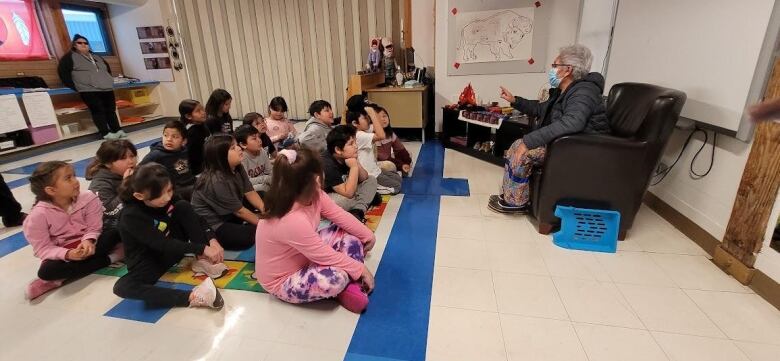 An elder sits in a chair facing a class of students seated on the floor. 