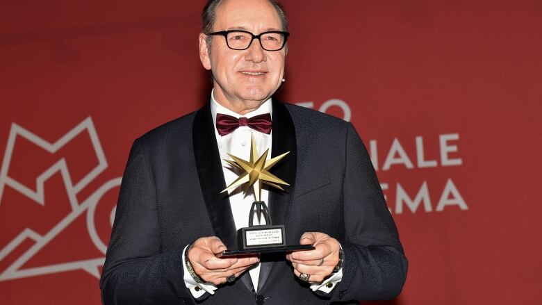 Man wearing glasses and a maroon bow tie holding a star shaped statue.