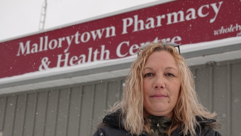 A woman with blonde hair stands in the snow in front of a burgundy pharmacy sign.