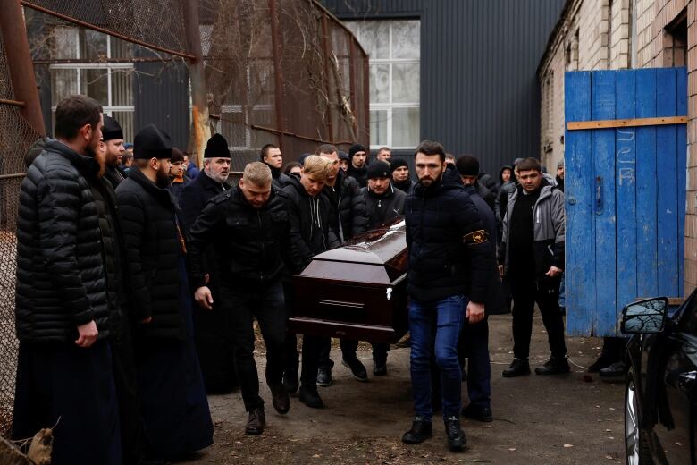 Pallbearers and onlookers surround a coffin in an outdoor setting.