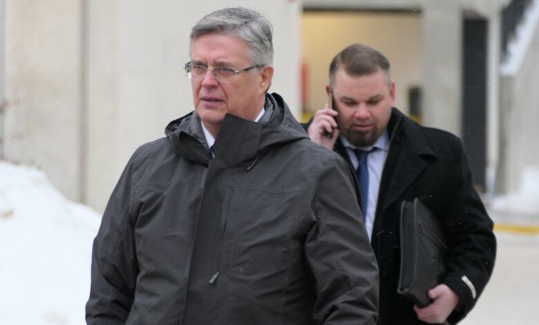 A man in a parka with grey hair is shown above the waste, standing outside on a snowy day.