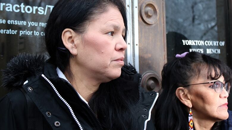 Two women stand side by side looking away from the camera outside a courthouse in Yorkton, Sask. 