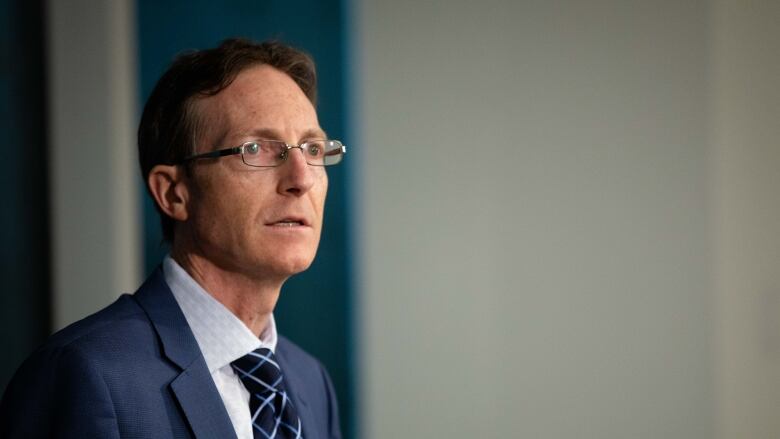 A man wearing a blue suit and glasses speaks at a podium.