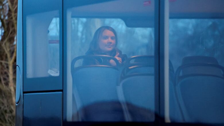 A young woman is seen through a window, sitting at the back of a bus.