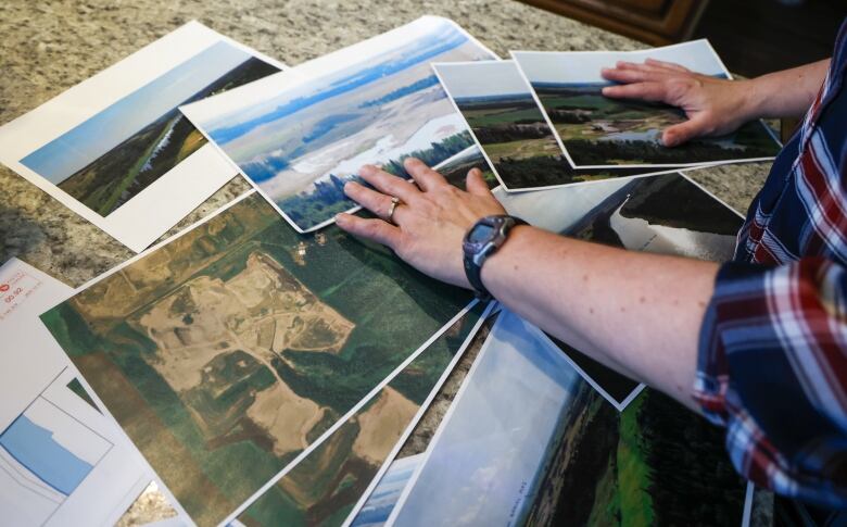 A series of photographs are fanned out on a countertop show aerial images of agricultural land and gravel pit operations.