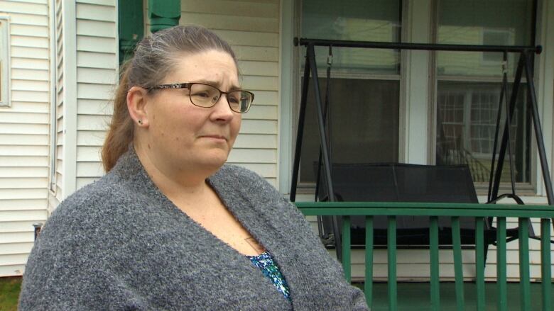 A woman looks concerned, standing in front of a house. 