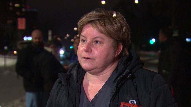 A woman speaks to a reporter outside the hospital Tuesday night, wearing a sticker against mandatory overtime.